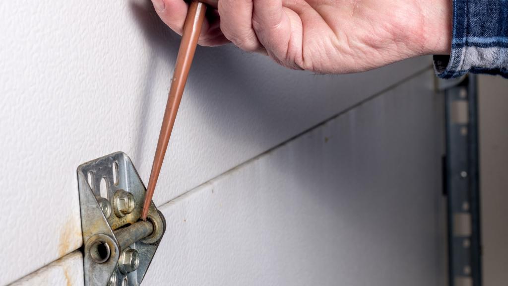 Applying lubricant to hinges during winter garage door maintenance