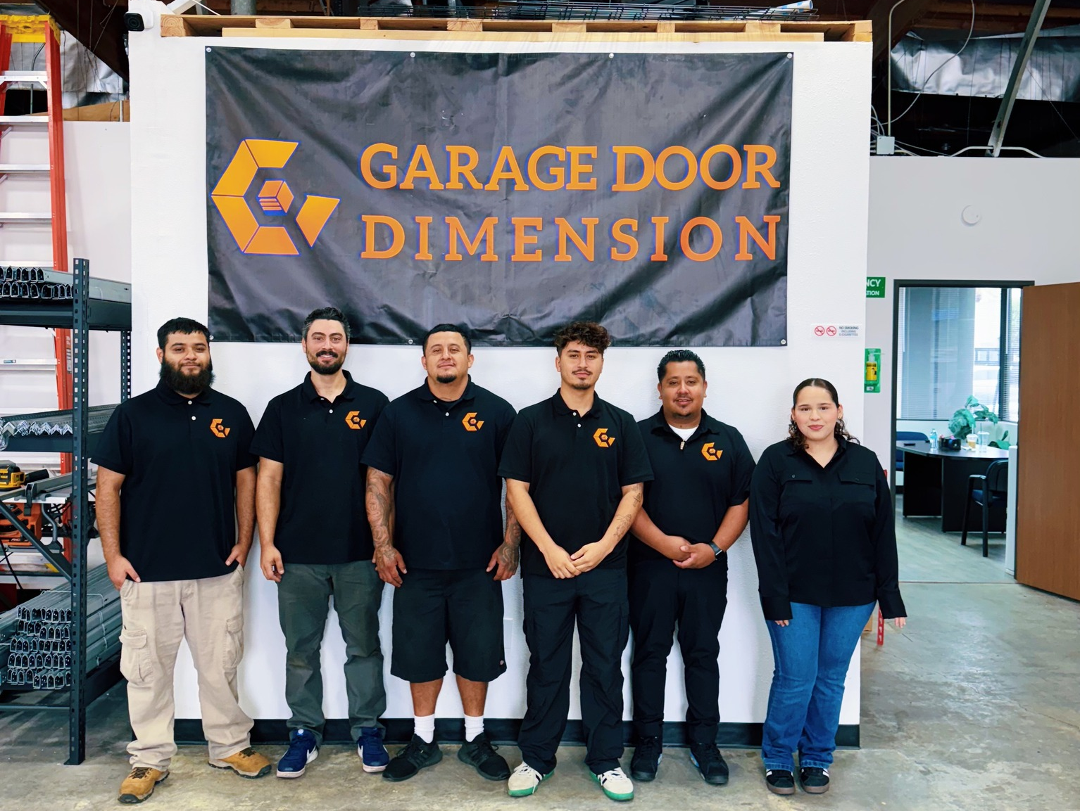 Team of six Garage Door Dimension employees in black polo shirts standing in front of a company banner, showcasing their commitment to quality garage door parts and services in Santa Ana, California.