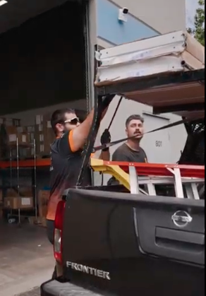 Two garage door technicians loading garage door panels onto the service truck at the Garage Door Dimension warehouse.